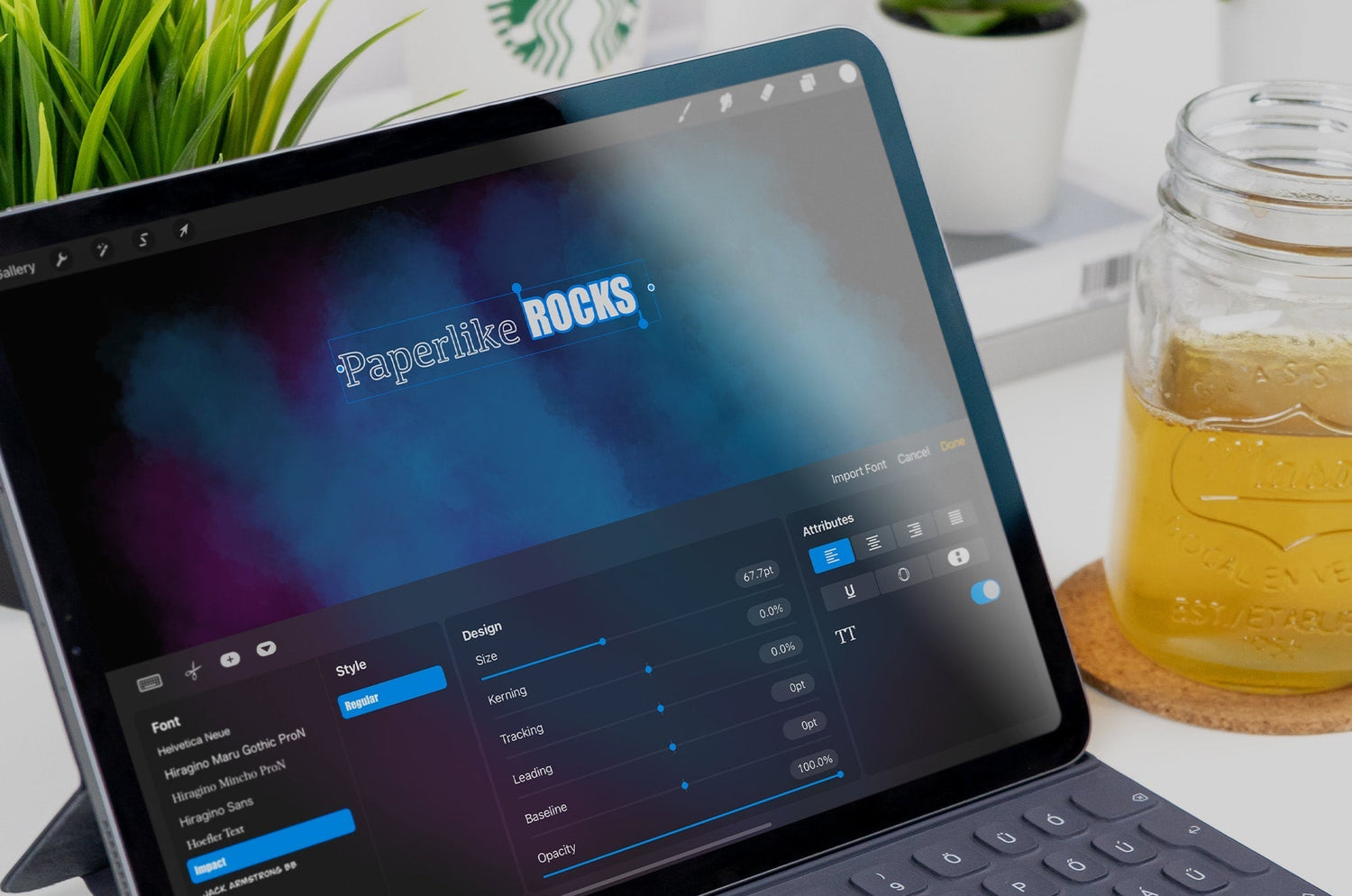 Close-up of an iPad on a desk with a keyboard case, showing a digital design app where text reads ‘Paperlike ROCKS.’ A mason jar with iced tea and a potted plant sit beside it.