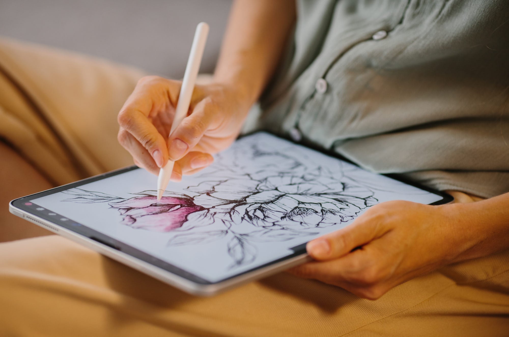 Close-up of a person using an Apple Pencil on an iPad to color a detailed floral illustration, shading a pink flower petal.