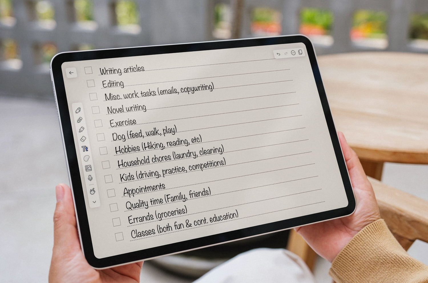 Person holding an iPad displaying a digital checklist with tasks including writing, editing, work emails, novel writing, exercise, chores, and family time.