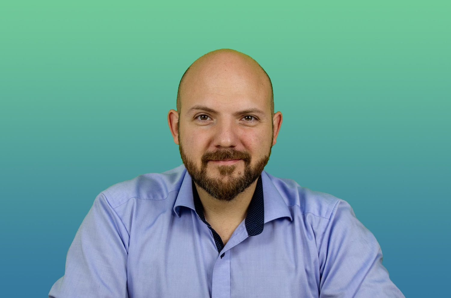 Man with beard and bald head wearing a light blue shirt, smiling against a green and blue gradient background.