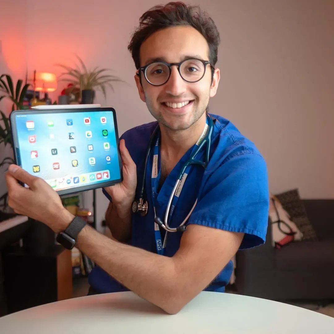 A man in scrubs with a stethoscope around his neck presents his Apple iPad. An Apple Pencil attached to show the top of the tablet. Apps and icons are visible on the screen.