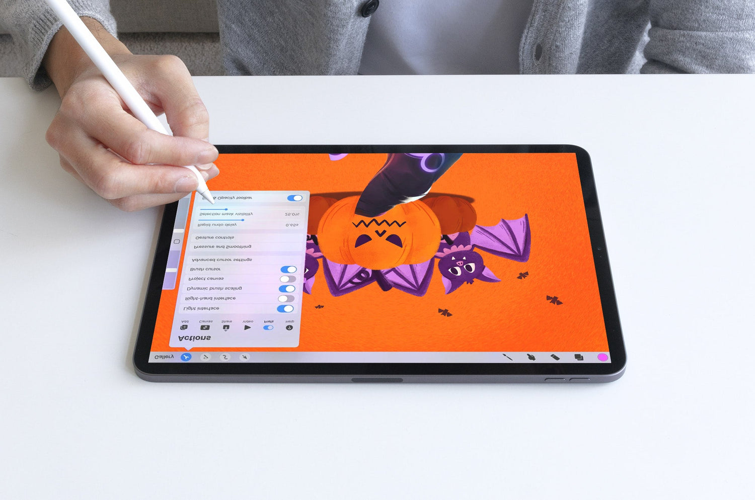 Person using an Apple Pencil on an iPad to draw a Halloween illustration of a pumpkin with bats on an orange background.