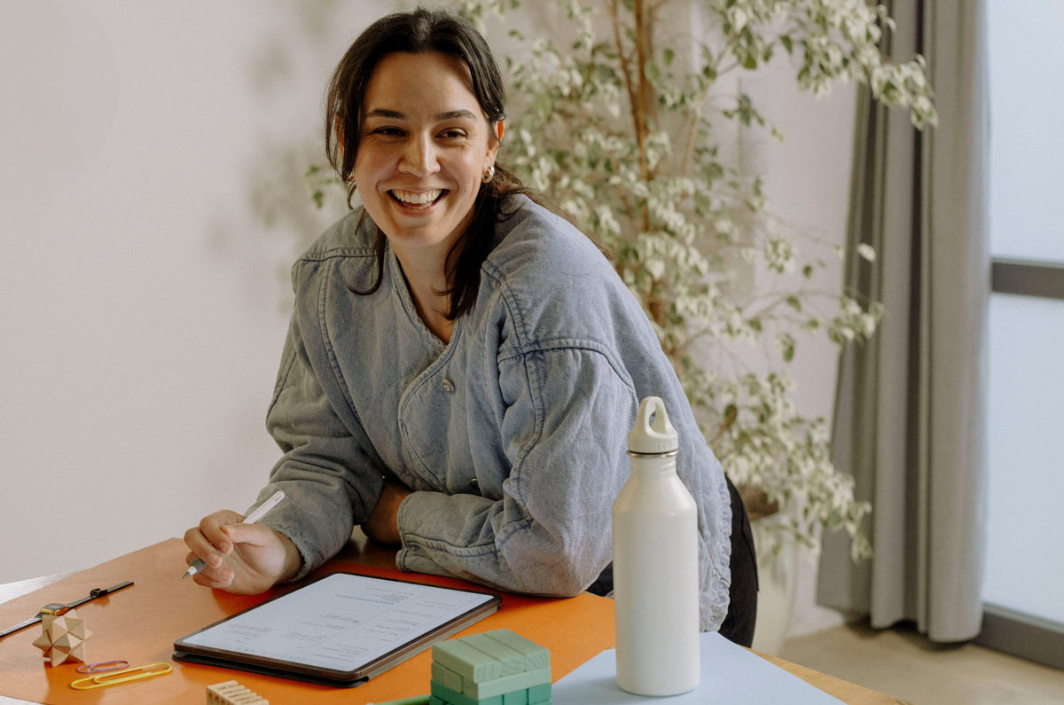 A woman sits at a desk, holding an Apple Pencil over an iPad.