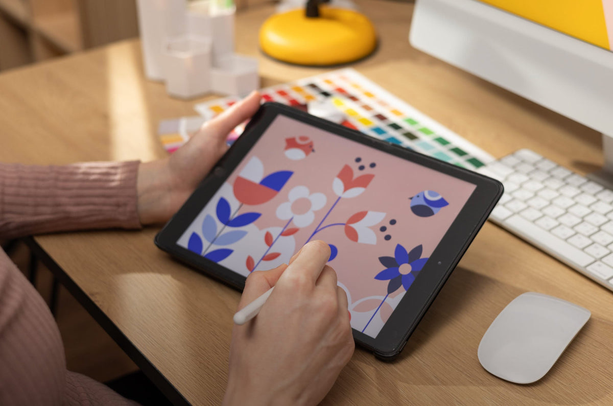 Someone sitting at a desk, holding an iPad in one hand while drawing on it with an Apple Pencil in the other hand.