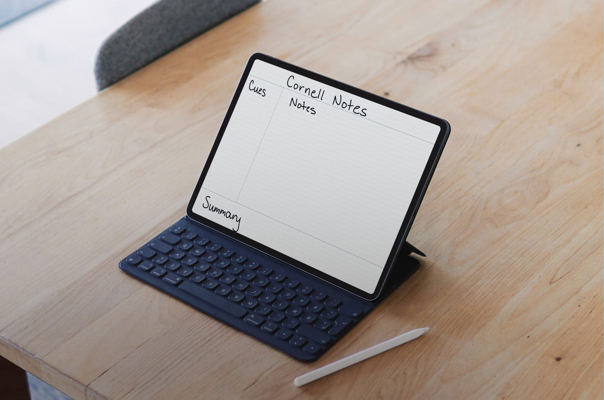 An iPad propped up with a keyboard case on a wooden desk with an Apple Pencil next to it and Cornell notes open on the screen.
