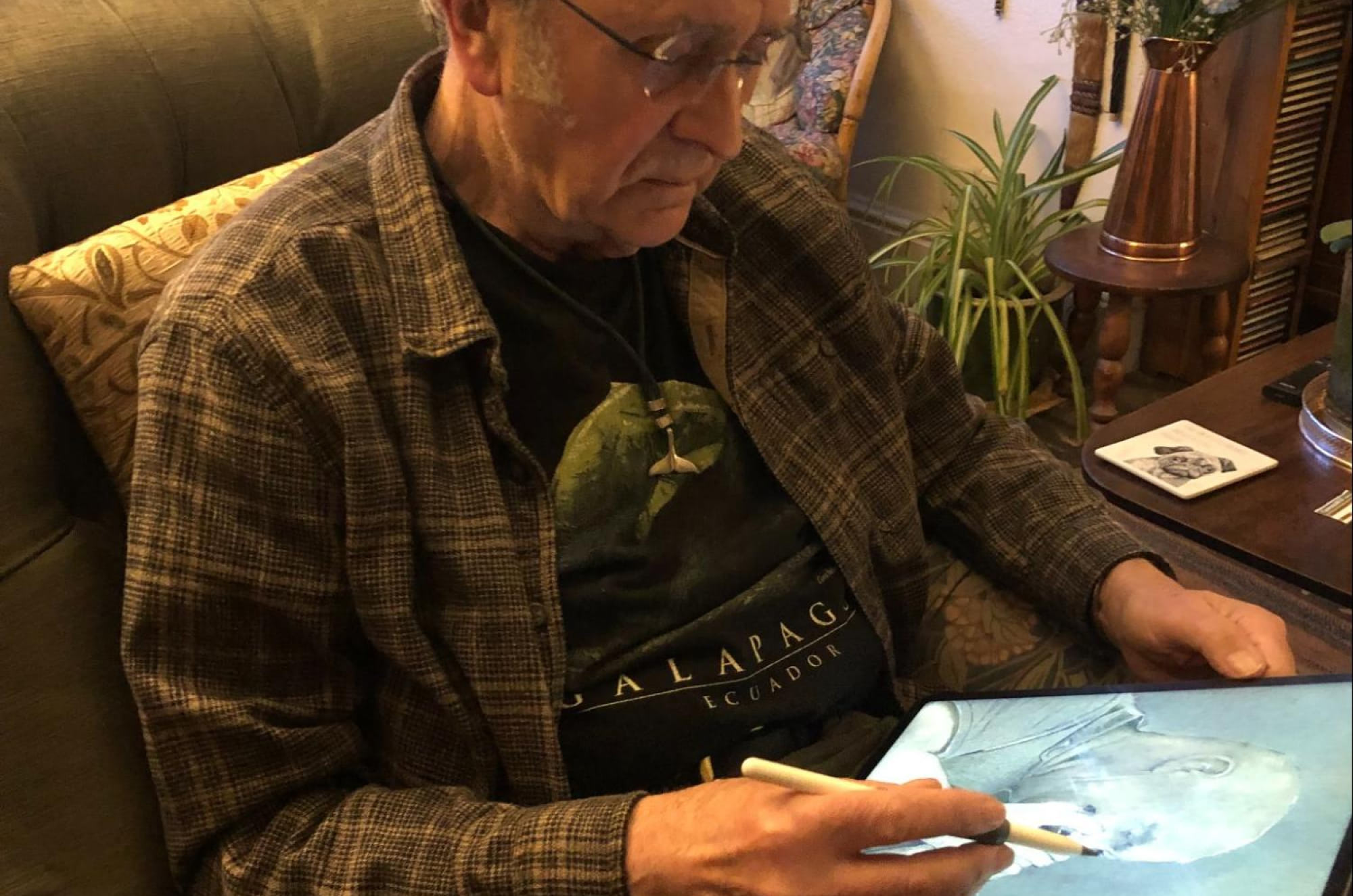 A man sitting on a couch, sketching on an iPad with an Apple Pencil.