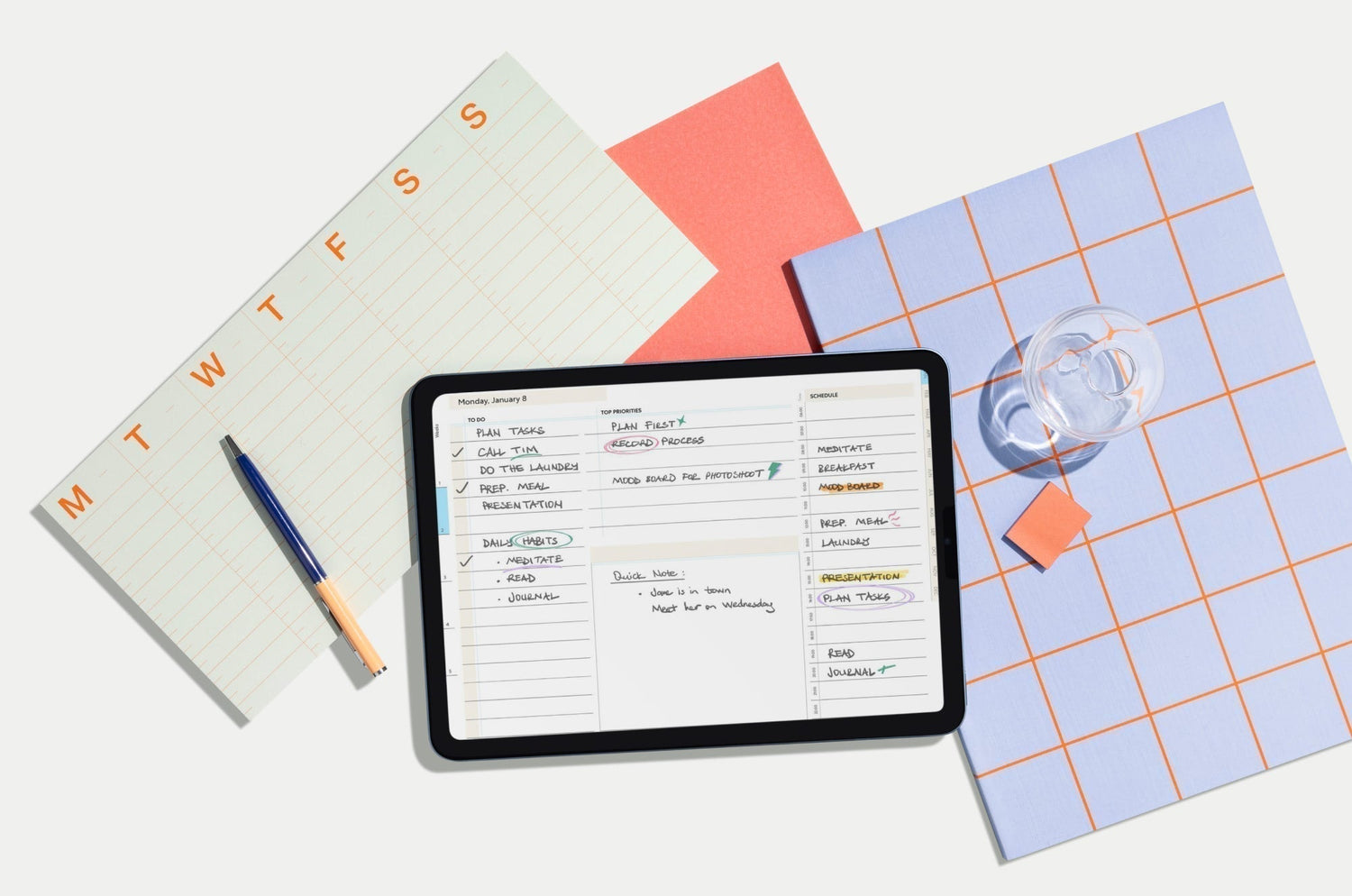 An iPad with a bullet journal on the screen, surrounded by graph papper, a water bottle, and other accessories.