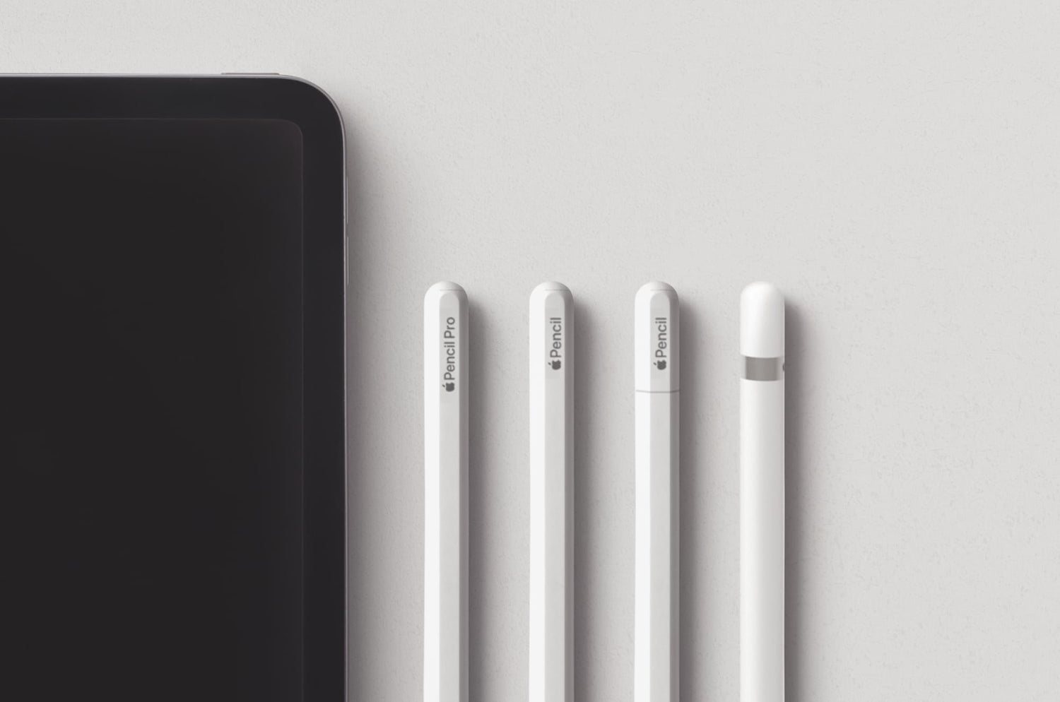 Four generations of Apple Pencil lined up beside an iPad, including Apple Pencil Pro and previous models.