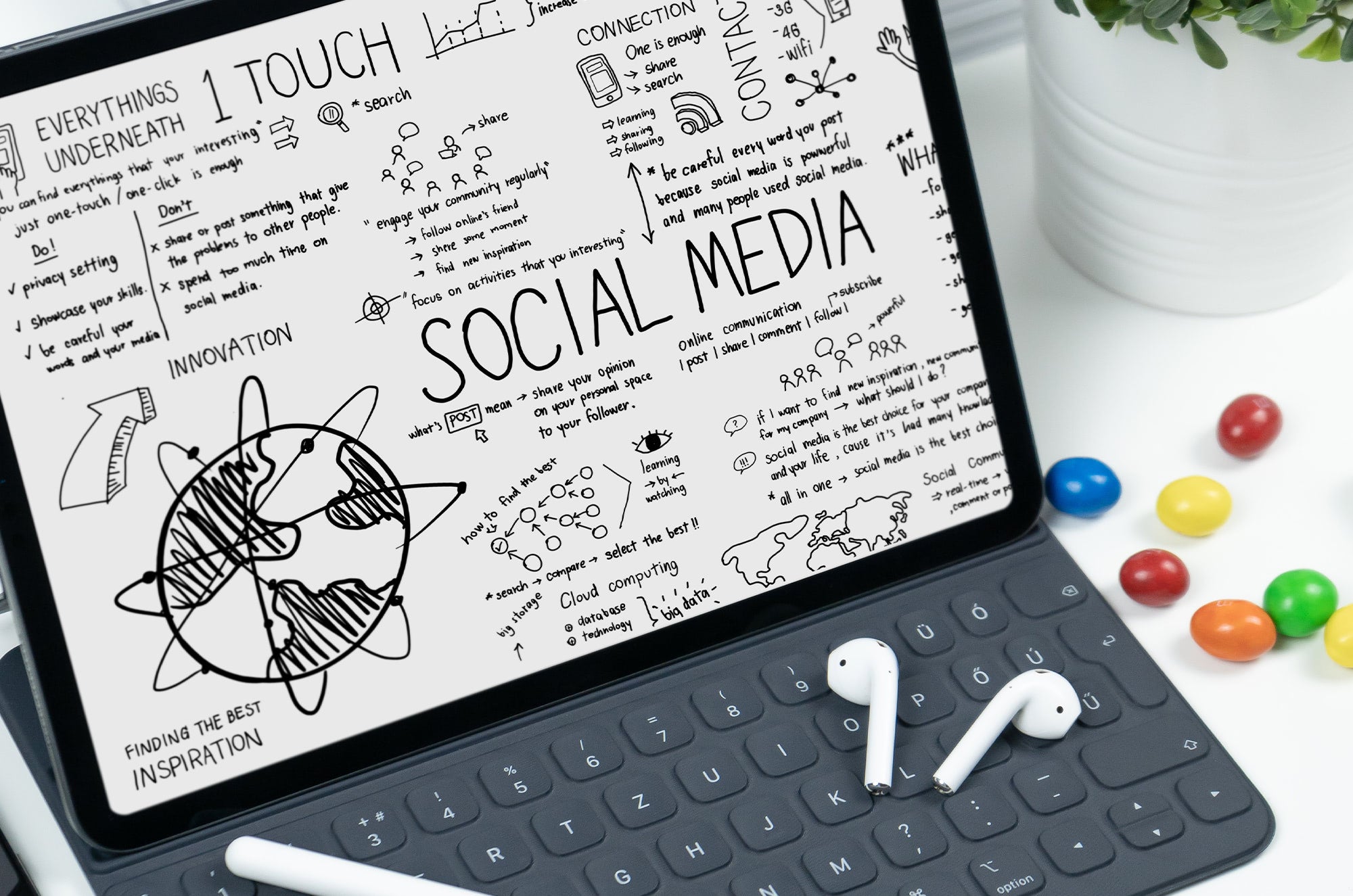 iPad on a keyboard stand displaying handwritten digital notes and sketches about social media, with doodles, diagrams, and keywords, next to wireless earbuds and colorful candy.