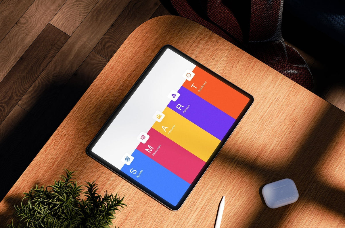 iPad on wooden desk displaying a colorful SMART goals chart with categories Specific, Measurable, Achievable, Relevant, and Time-Bound.