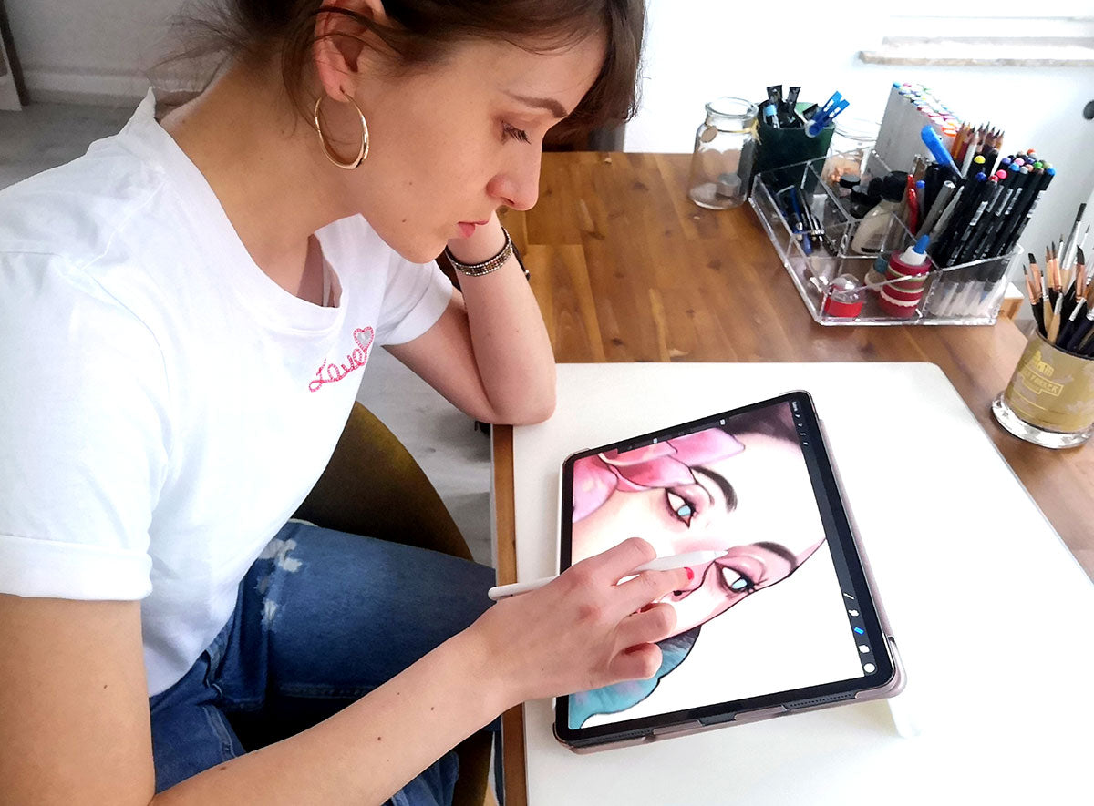 Digital artist using an Apple Pencil to draw a detailed portrait on an iPad at a wooden desk with art supplies.