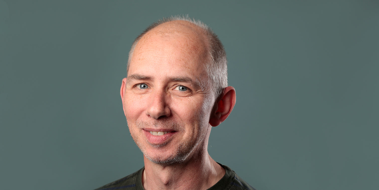 Portrait of a smiling man with short gray hair against a plain background.