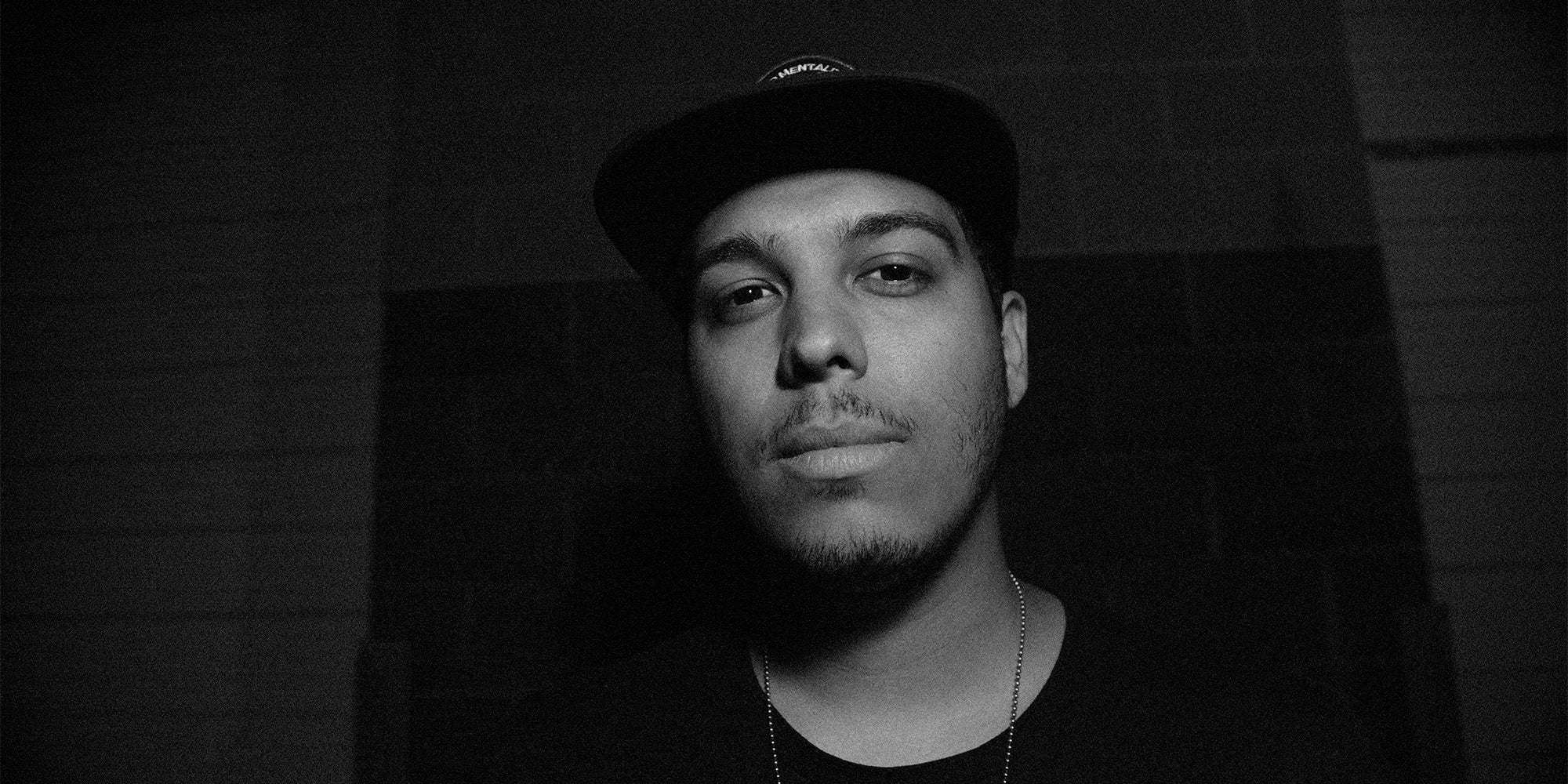 Black and white portrait of a man wearing a cap, looking directly into the camera.”