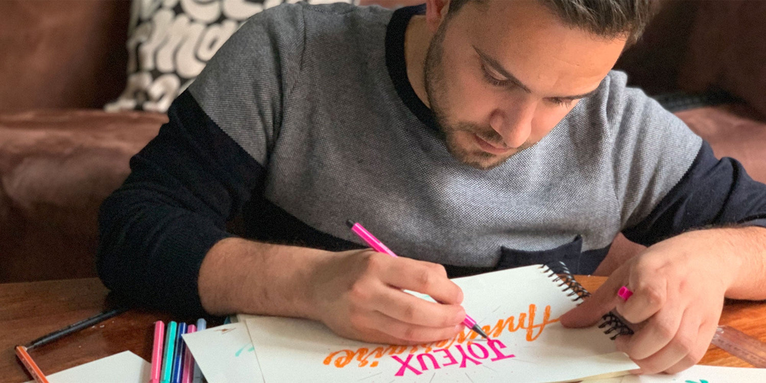 Man focused on hand lettering with colorful markers in a sketchbook.